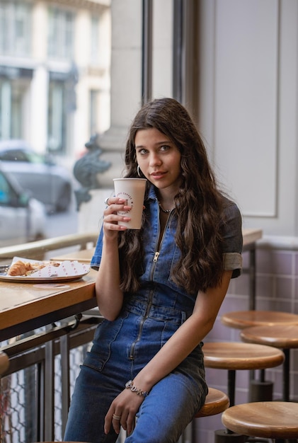 Meisje in een coffeeshop met een kopje koffie bij het raam. Model in een café met koffie. het meisje