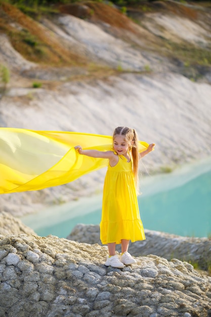 Meisje in een gele jurk met vleugels in een gele doek bij het meer