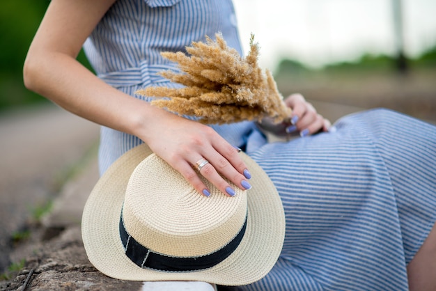 Meisje in een gestreepte jurk met hoed en korenaren zittend op spoorlijnen