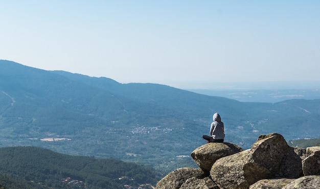 Meisje in een grijze hoodie zittend op een rots van een klif kijken naar het berglandschap dat zich uitstrekt tot aan de horizon