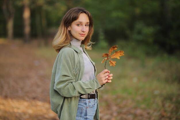 meisje in een groen shirt en spijkerbroek in het herfstbos meisje met een esdoornblad in haar handen