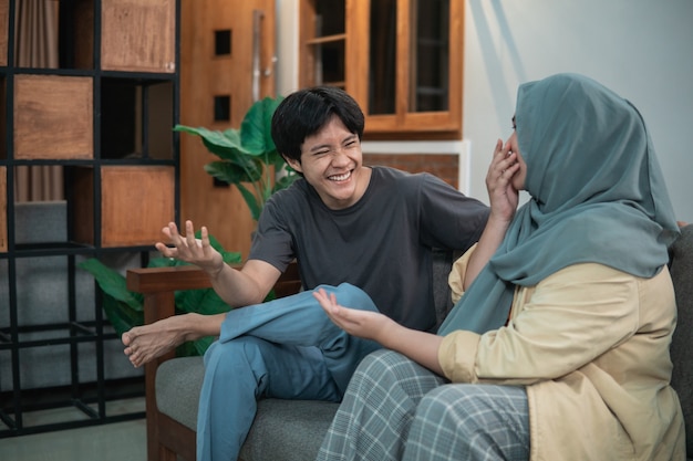 Meisje in een hijab en een man lachen vrolijk in de woonkamer zittend op een houten stoel