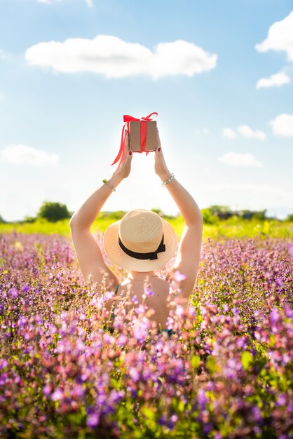 Foto meisje in een hoed heeft een geschenk met een rood lint in haar handen. vicia cracca in de zomer in het veld. bloemen bloeien. concept vakantie, natuurlijke geschenken.