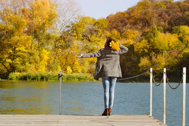 Meisje in een hoed met bladeren in handen die op het dok staan Herfst zonnig Achteraanzicht