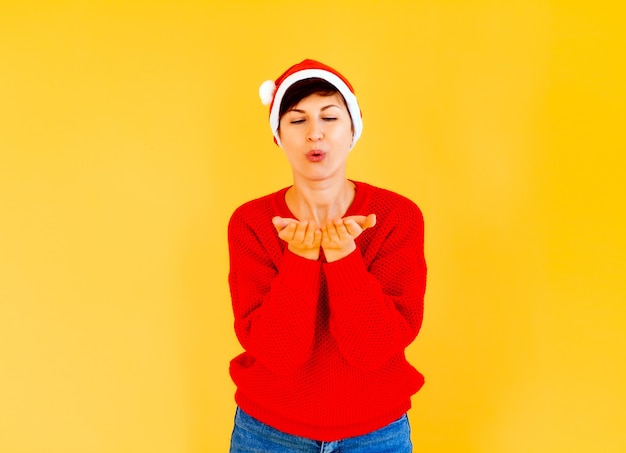 Meisje in een kerstmuts en een rode trui op een gele achtergrond met een emotioneel gezicht