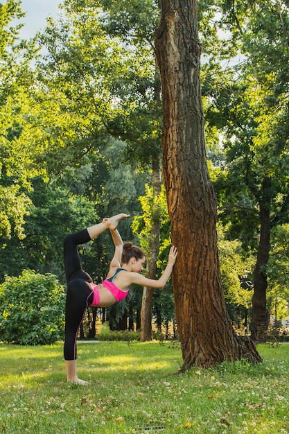 meisje in een licht trainingspak doet 's middags in de zomer yoga in het park