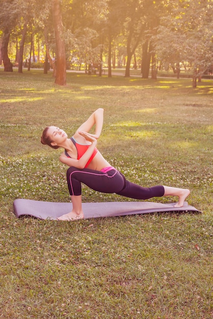 meisje in een licht trainingspak doet 's middags in de zomer yoga in het park