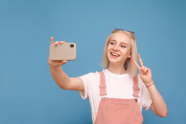 meisje in een lichte casual kleding maakt selfie op blauwe muur