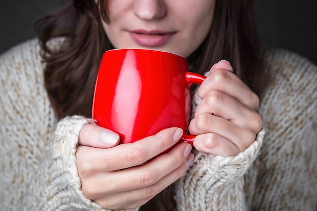 Meisje in een lichte trui met een rode kop koffie