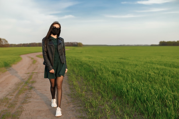 meisje in een medisch masker loopt of loopt op een groen veld. Lente zomer in quarantaine. coronavirus. COVID 19.