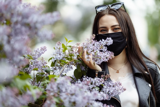 Meisje in een medisch masker met bloeiende sering in het park. Zwarte masker. Coronavirus bescherming. Lente allergie