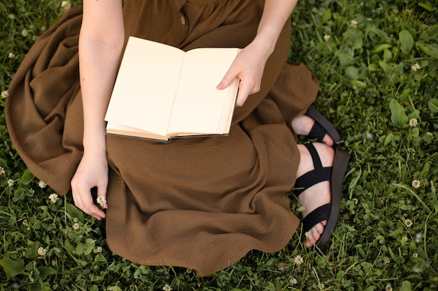 Meisje in een olijfjurk met een boek met een blanco pagina in haar handen zittend op het groene gras