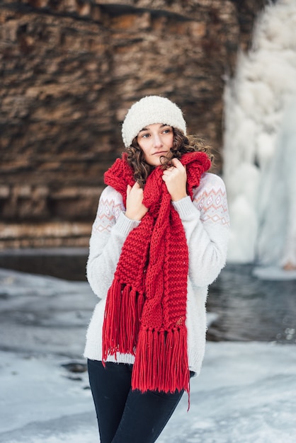 meisje in een rode sjaal in de winter in de buurt van de waterval