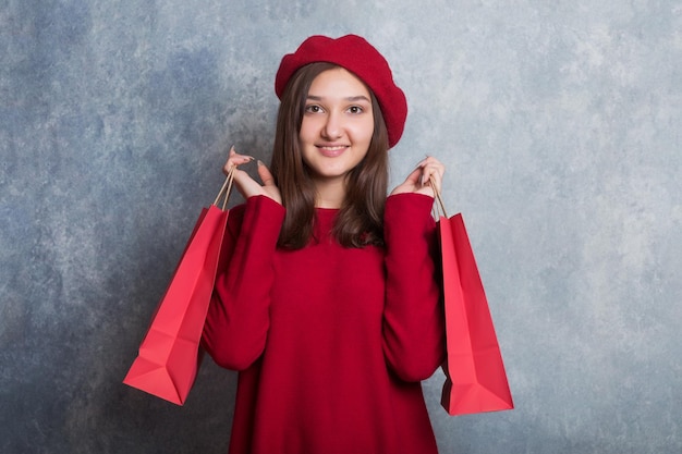 meisje in een rode trui en een baret houdt rode papieren boodschappentassen in haar handen