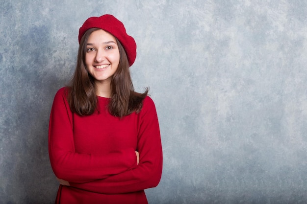 meisje in een rode trui en een baret tegen de achtergrond van een moderne grijze muur in loftstijl