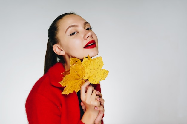 Meisje in een rode trui met rode lippenstift raakt speels haar gezicht aan met een esdoornblad