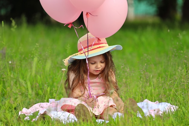 Meisje in een roze jurk met een hoed zit op het gras in het park. Hoge kwaliteit foto