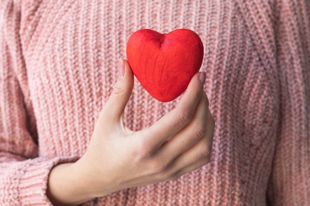 Meisje in een roze trui houdt een rood hart in haar hand, het concept van een liefdesverklaring.