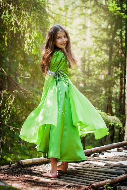 Meisje in een sprookjesachtige elfjesjurk loopt blootsvoets langs een bospad en draait zich om