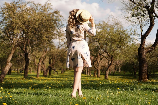 Meisje in een strohoed in de tuin. Achteraanzicht. Trendy casual zomer- of lente-outfit