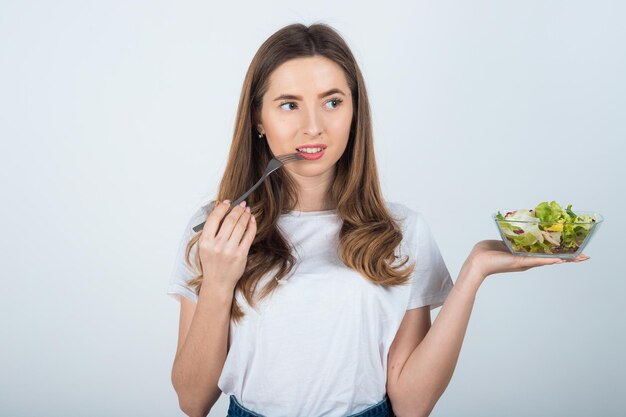 meisje in een wit t-shirt houdt een kom salade in haar handen en eet