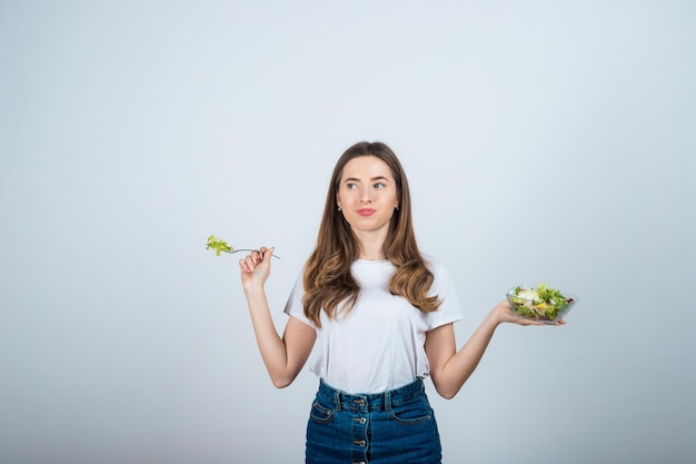 meisje in een wit t-shirt houdt een kom salade in haar handen en eet