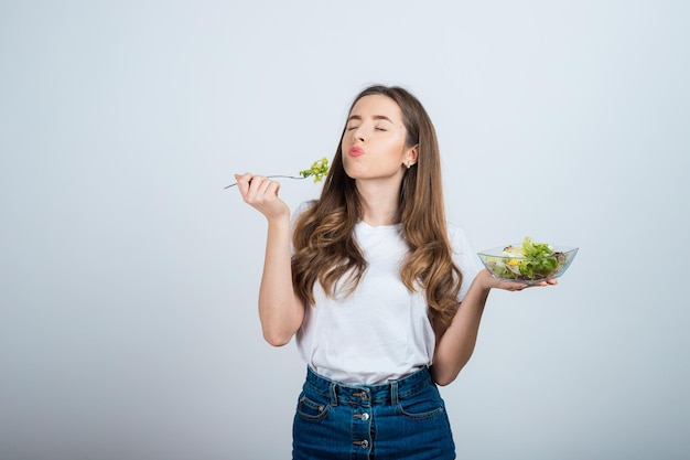 meisje in een wit t-shirt houdt een kom salade in haar handen en eet