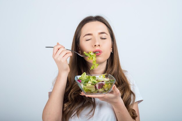 meisje in een wit t-shirt houdt een kom salade in haar handen en eet