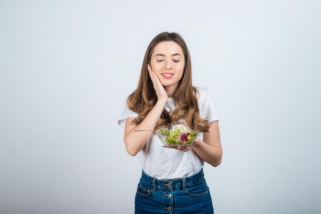 meisje in een wit t-shirt houdt een kom salade in haar handen en eet