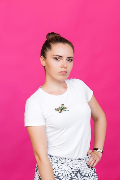 Foto meisje in een wit t-shirt poserend met een brochevorm van libel met blauwgroene edelsteenimitatie op roze achtergrond
