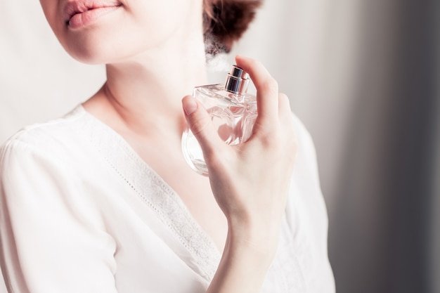 Meisje in een witte jurk spuit zichzelf parfum in haar nek