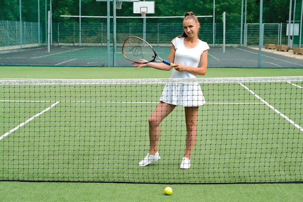 Meisje in een witte sportjurk op de tennisbaan, tennisbaan en racket