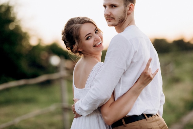 Meisje in een witte zomerjurk en een man in een wit overhemd op een wandeling bij zonsondergang met een boeket in een dorp buiten de stad