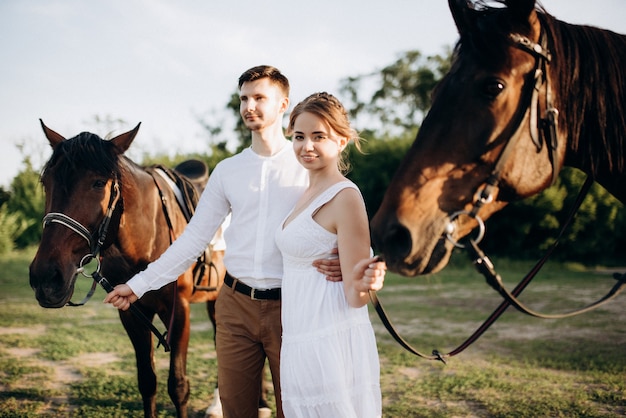 Meisje in een witte zomerjurk en een man in een wit overhemd op een wandeling met bruine paarden in het dorp