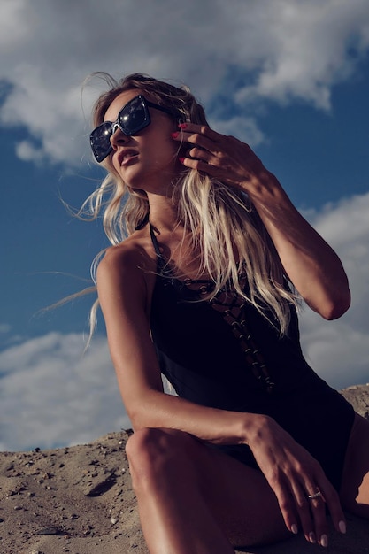 Meisje in een zwart zwempak en zonnebril zit op het zand te zonnebaden en te genieten van een zomerdag