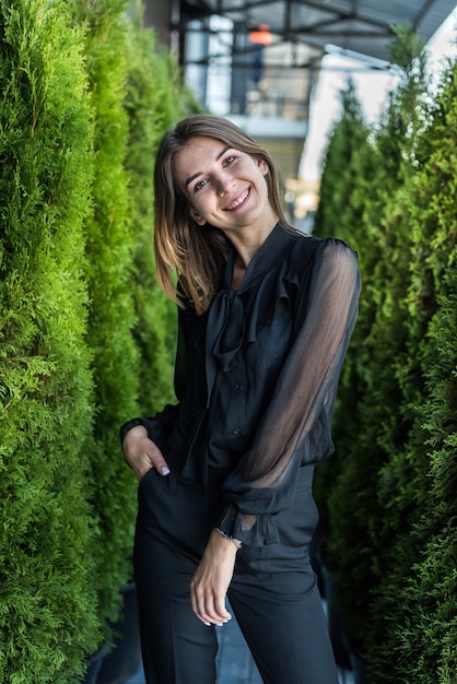 Meisje in een zwarte elegante jurk poseren tussen dennennaalden en genieten van een warme zonnige dag