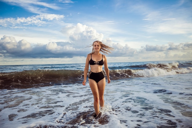 Meisje in een zwarte zwembroek loopt langs de oceaan