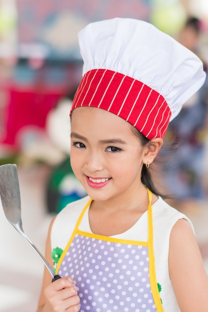 Foto meisje in eenvormige chef-kok met gietlepel