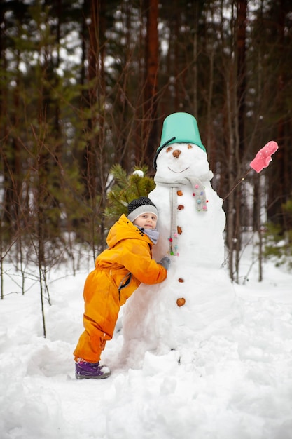 Meisje in gele jumpsuit in de winter in bos dichtbij sneeuwman