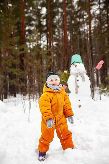 Meisje in gele jumpsuit in de winter in bos dichtbij sneeuwman