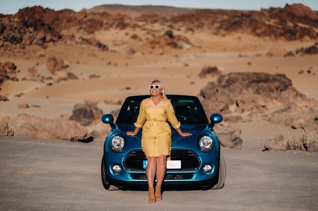 Meisje in gele jurk genieten van een roadtrip in een cabriolet door een verlaten vallei met bergen, Canarische eilanden, Tenerife.