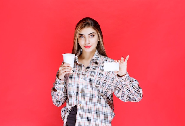 Meisje in geruit overhemd met een koffiekopje en haar visitekaartje