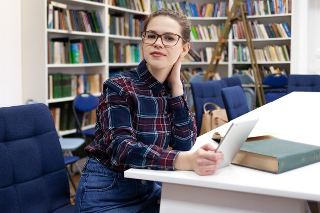 Meisje in glazen die met tabletzitting werken in bibliotheek.