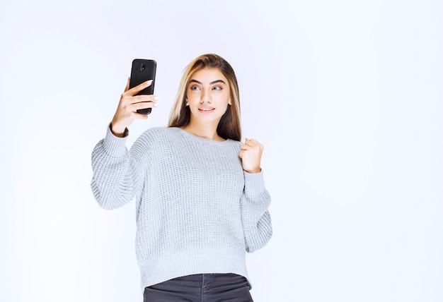 Meisje in grijs sweatshirt met een zwarte smartphone en tevreden.