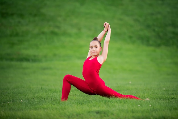 Meisje in heldere rode overall turnen op het gras in het park