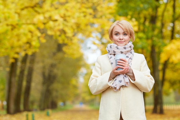 Meisje in het herfstpark drinkt heerlijke thee in de herfst in het herfstverkoopconcept van het park