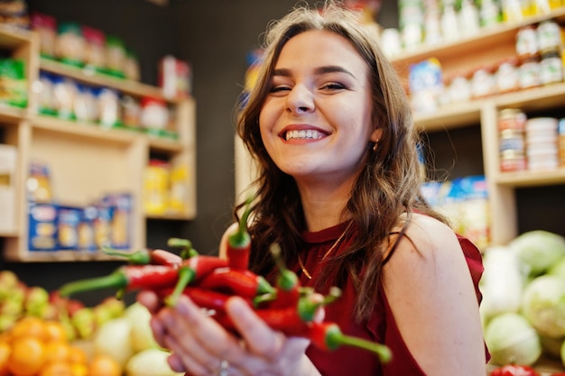 Meisje in het rood met hete chilipepers in de fruitwinkel