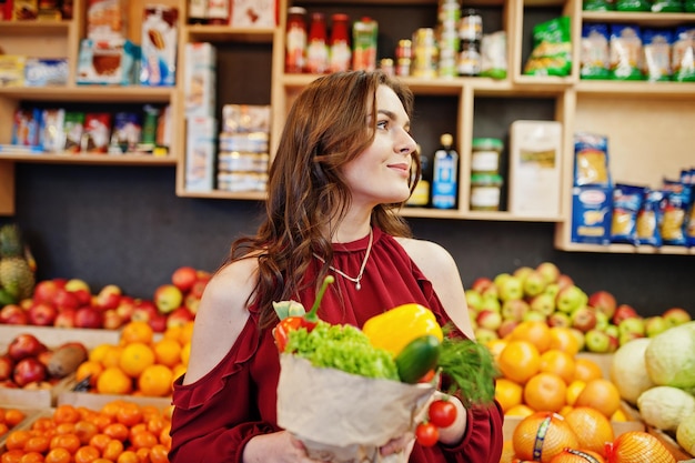 Meisje in het rood met verschillende groenten in de fruitwinkel