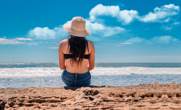 Meisje in hoed zitten met haar rug naar de zee kijken Jonge vrouw in hoed zitten met haar rug kijken naar de zee vakantie meisje concept achteraanzicht van een meisje kijkend naar de zee