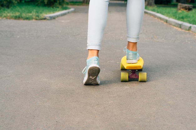 Meisje in jeans en sneakers rijden op een skateboard in het park